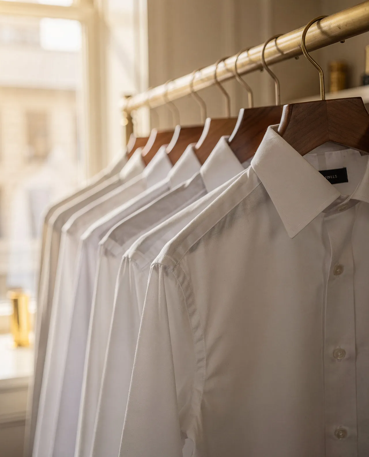 Freshly pressed white shirts on warm wooden hangers in a sunlit boutique